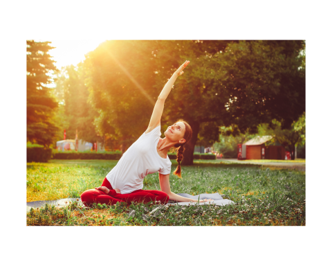 Young woman does a sitting yoga pose on grass with sunset behind her