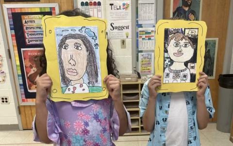 Two children hold diverse portraits in front of their faces.