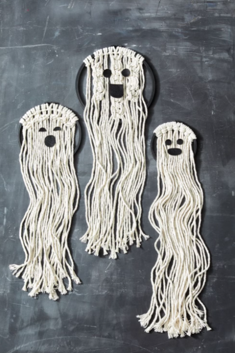 A picture of three ghosts made from painted black embroidery hoops and white macrame cord with felt eyes and mouths.